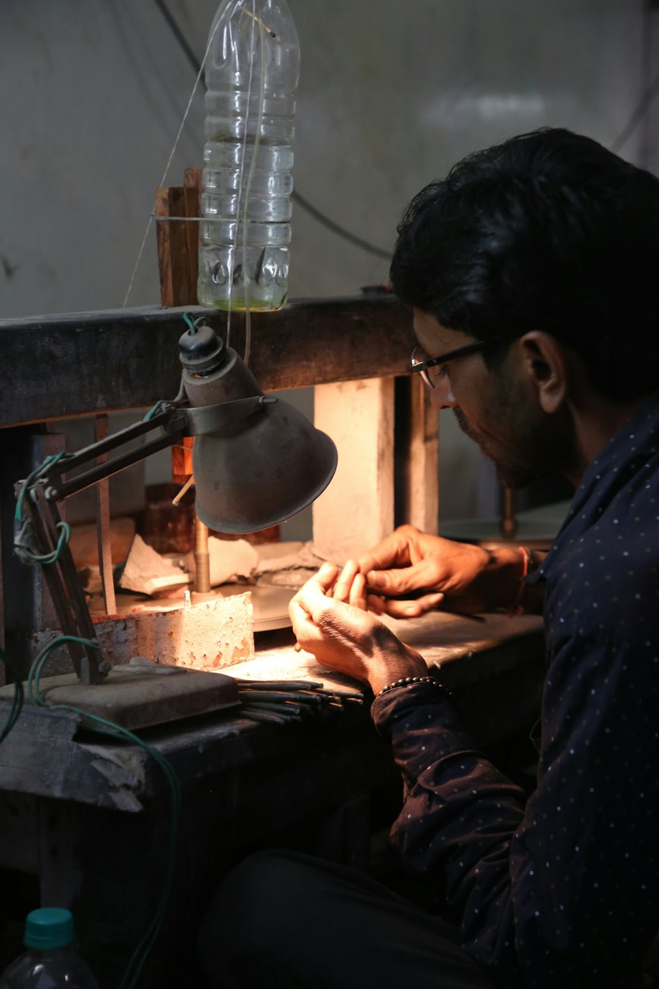 Ein Handwerker mit Brille arbeitet an einem detaillierten Gegenstand an einer Werkbank.