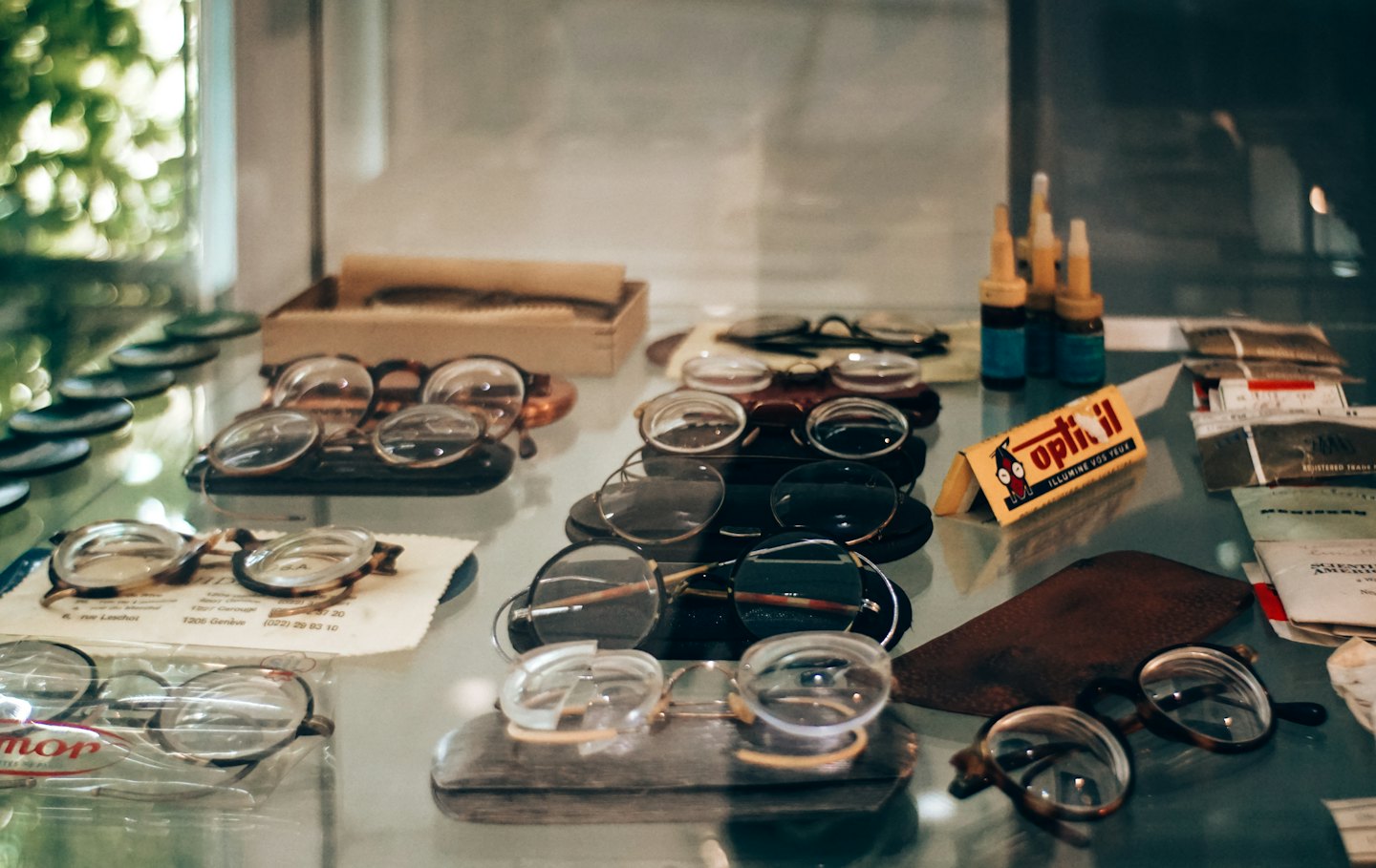 Eine Brille im Vintage-Stil und antike Accessoires stehen auf einem Glasregal.